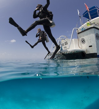 Over/under view showing divers performing giant stride entry into the clear calm waters of the Atlantic ocean.